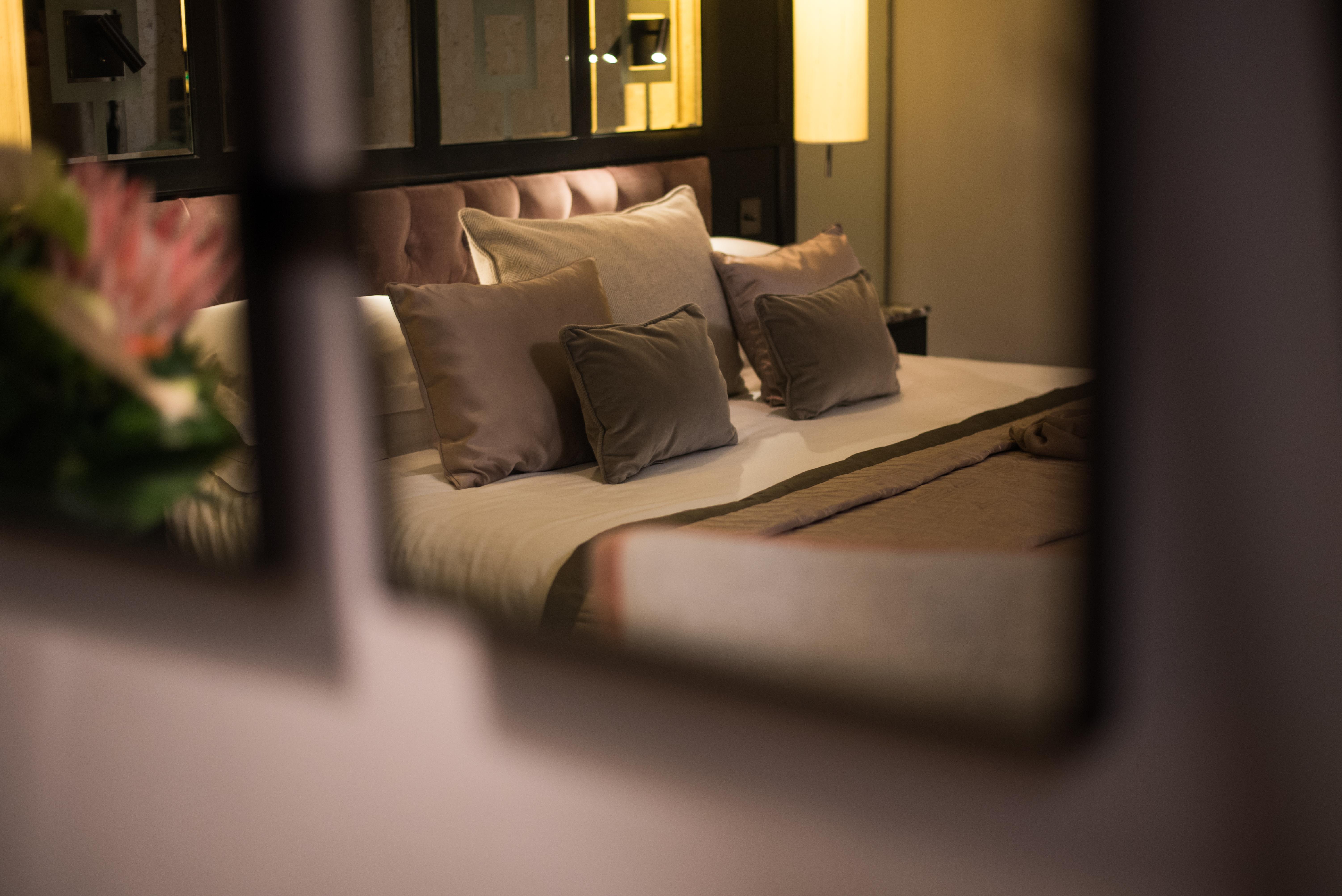 The Fitzwilliam Hotel Belfast Eksteriør bilde The photo shows a cozy and elegantly decorated bedroom. The focal point is a plush bed with soft, neutral-colored bedding and several decorative pillows arranged neatly on it. The room has a warm ambiance, enhanced by a standing lamp that provides so