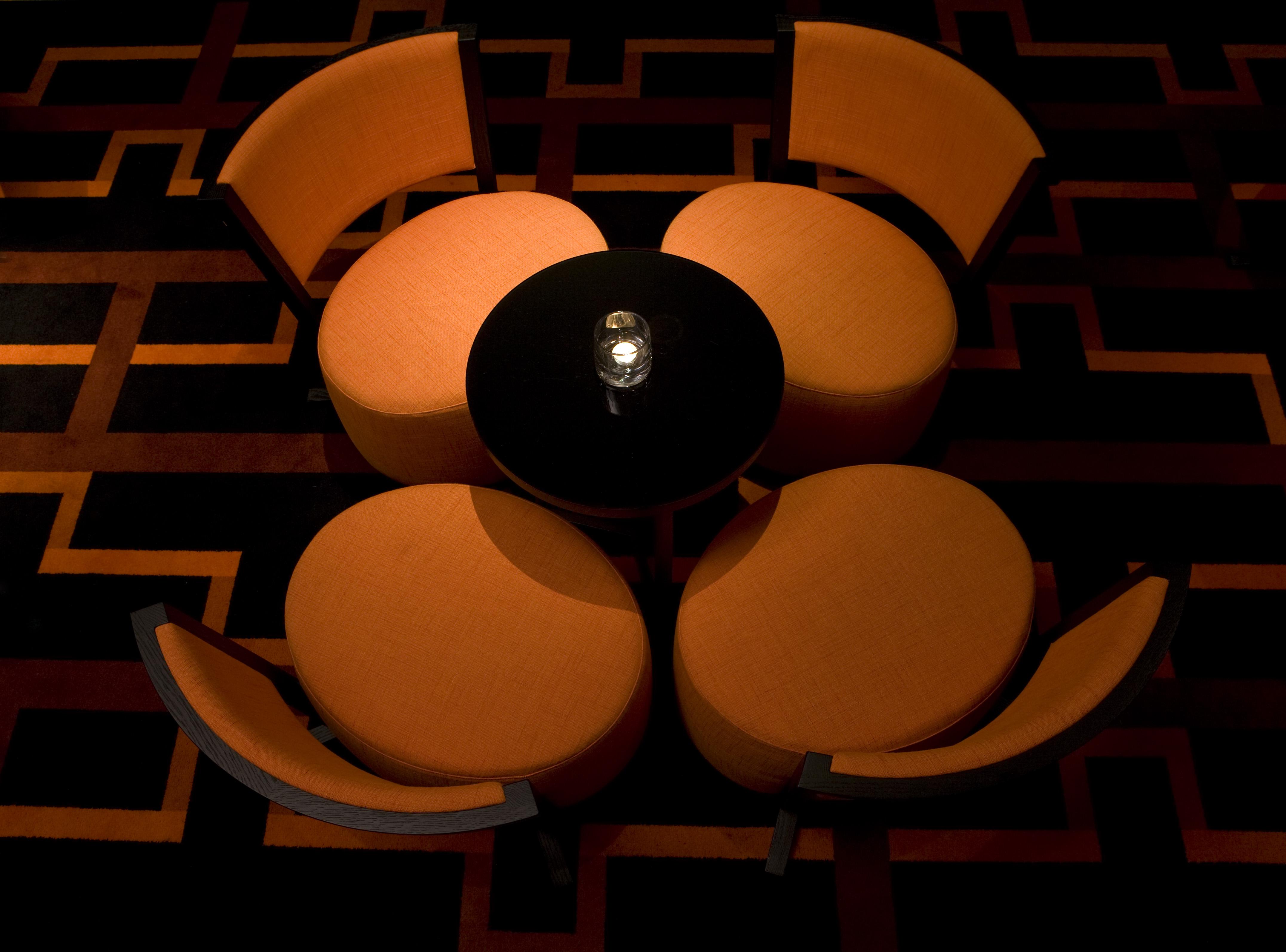 The Fitzwilliam Hotel Belfast Eksteriør bilde The image shows a small seating arrangement consisting of four orange chairs arranged around a circular black table. The setting appears to be in a dimly lit area, emphasizing the warm tones of the chairs and the dark finish of the table. The floor d