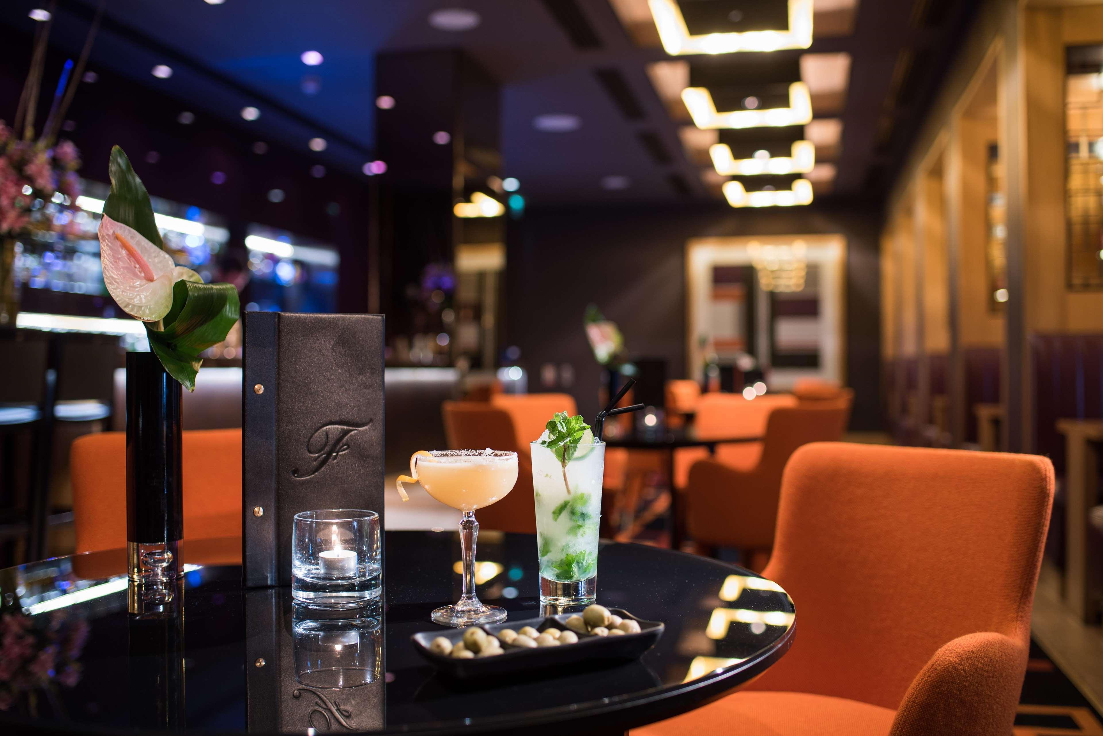 The Fitzwilliam Hotel Belfast Eksteriør bilde The photo depicts a stylish bar or lounge setting. There are two cocktails on a black table: one appears to be a light-colored drink garnished with a slice of fruit, while the other is a green cocktail possibly containing mint. A small plate of olive