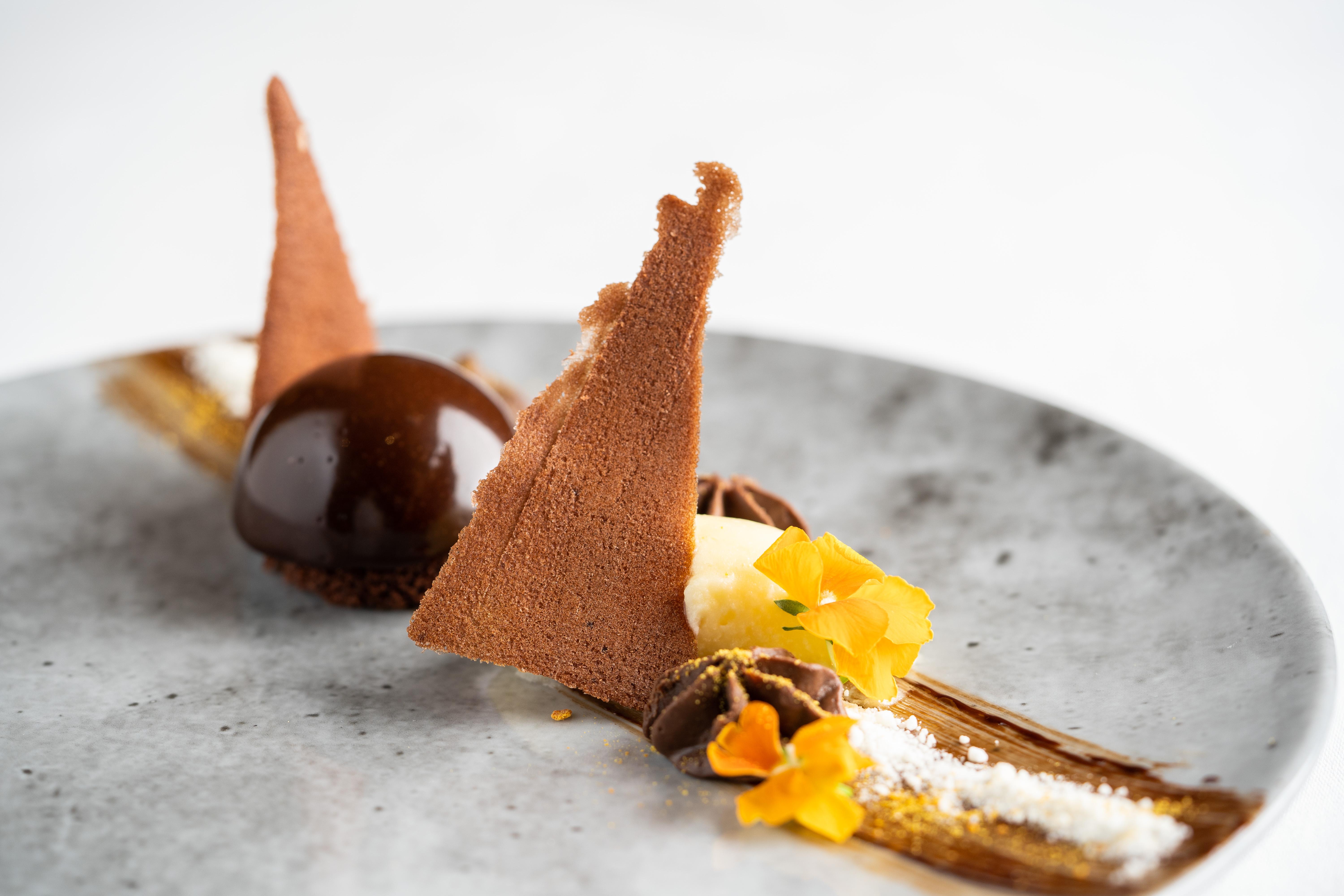 The Fitzwilliam Hotel Belfast Eksteriør bilde The photo displays an artfully plated dessert. It features a glossy chocolate sphere, accompanied by various chocolate components, including triangular chocolate tuile pieces that resemble sails. The plate is adorned with delicate garnishes such as y