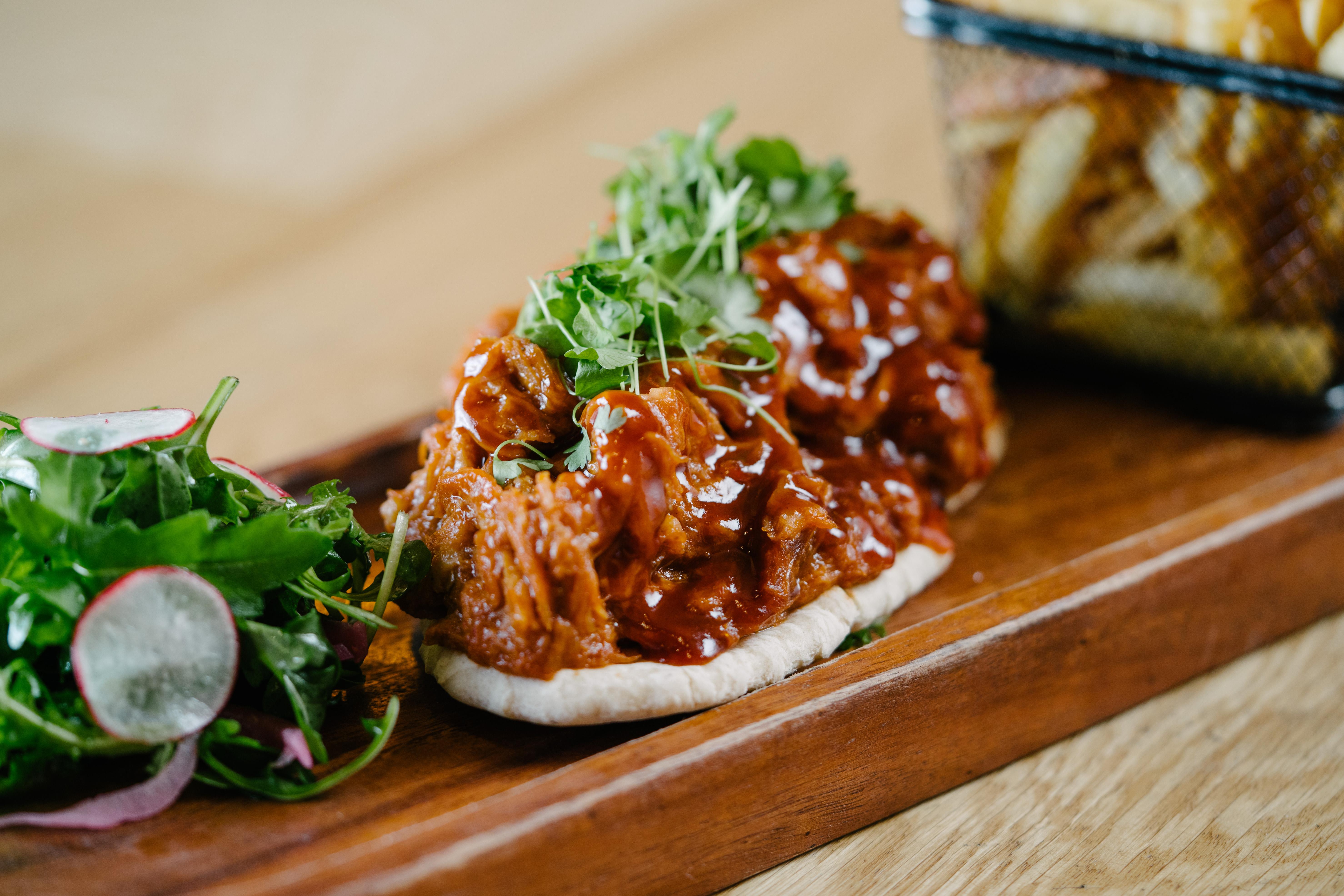 The Fitzwilliam Hotel Belfast Eksteriør bilde The photo shows a wooden platter featuring two pieces of bread topped with pulled meat covered in a rich barbecue sauce. The dish is garnished with fresh greens, including sprouts. On the side, there is a small serving of mixed salad with radishes an